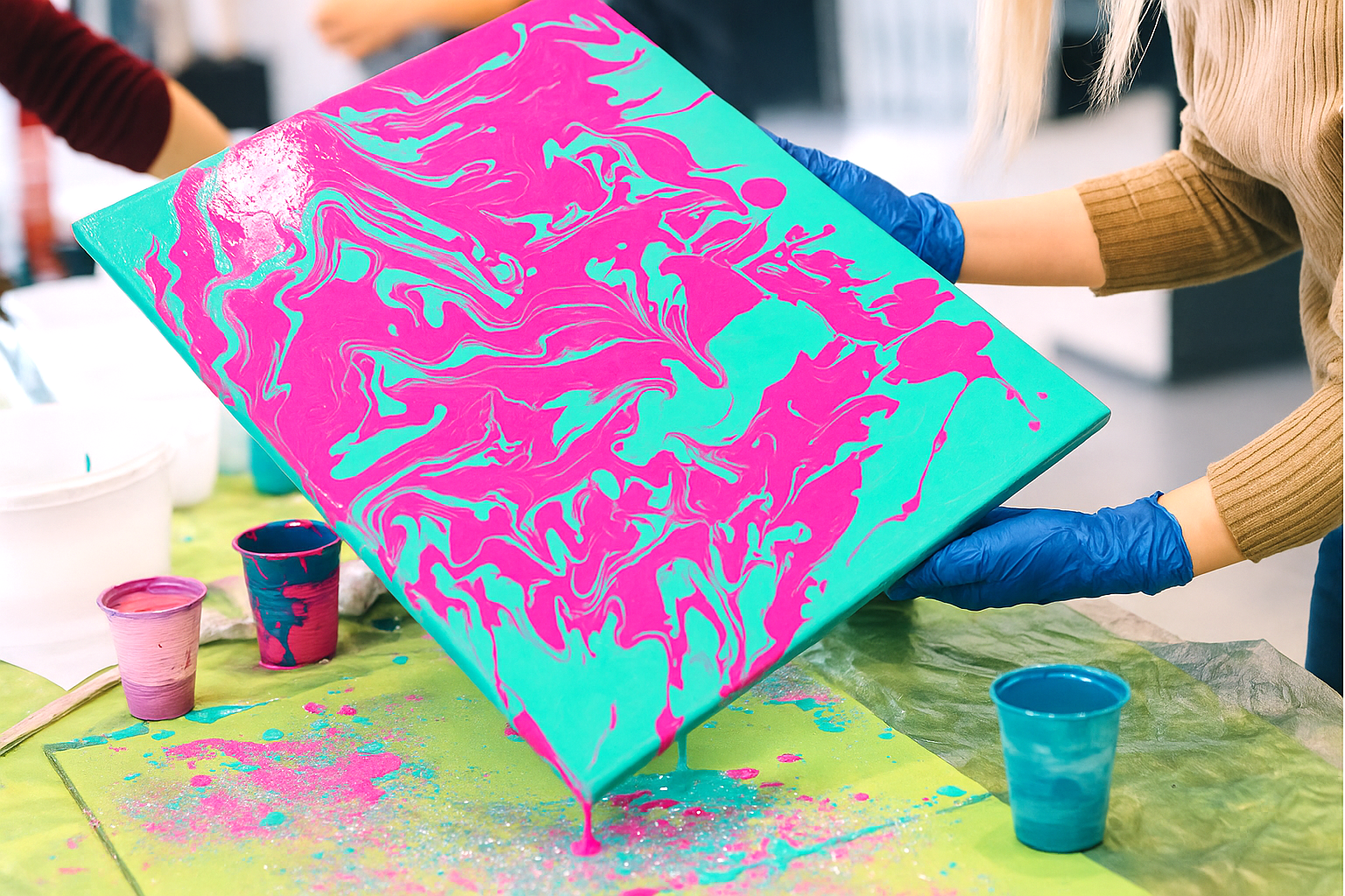 Hands holding teal and pink acrylic pour painting